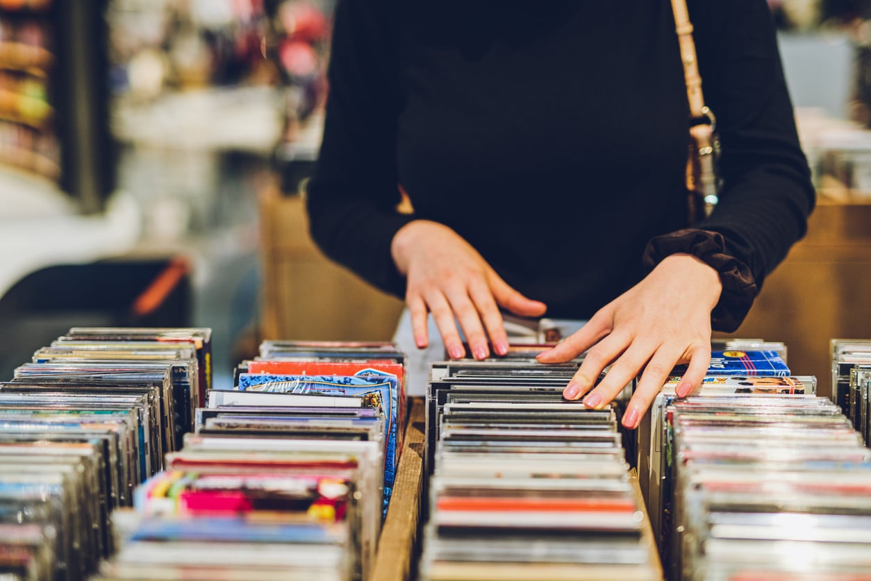 A person wearing a black long-sleeve top browses through rows of CDs in a store, using both hands to look through the selection.