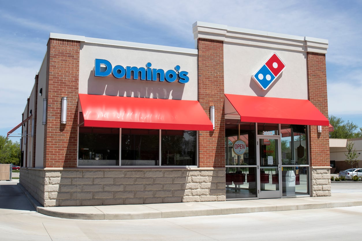 A Domino’s Pizza restaurant with red awnings and large windows, featuring the Domino’s logo and sign, stands out on a sunny day—an ideal spot for discovering Wild Fast-Food Facts while grabbing a slice.