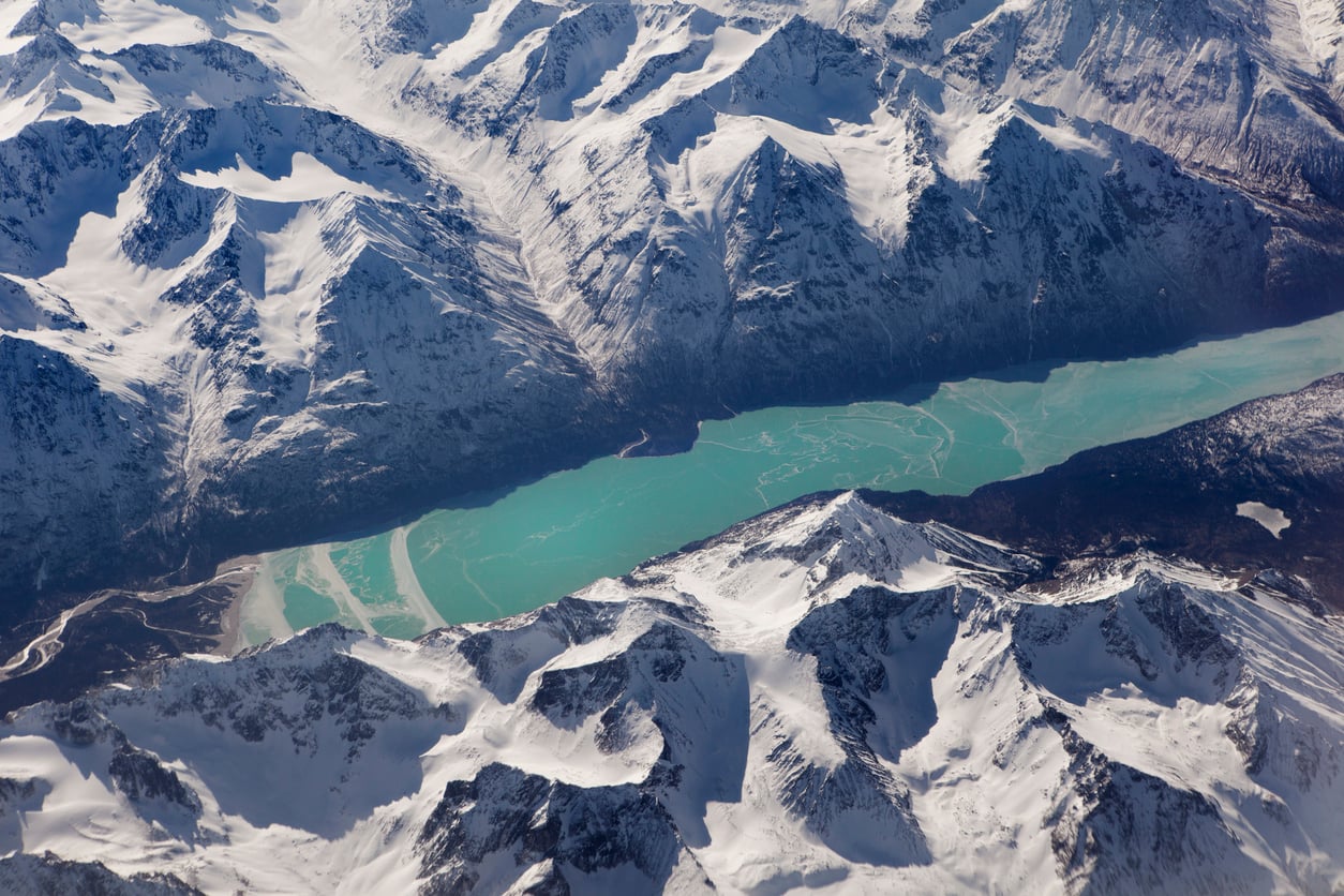A turquoise river winds through a snow-covered mountain range, with rugged peaks and valleys visible under a clear sky—scenes like these are just some of the breathtaking sights you can discover when exploring Travel Facts About The United States.