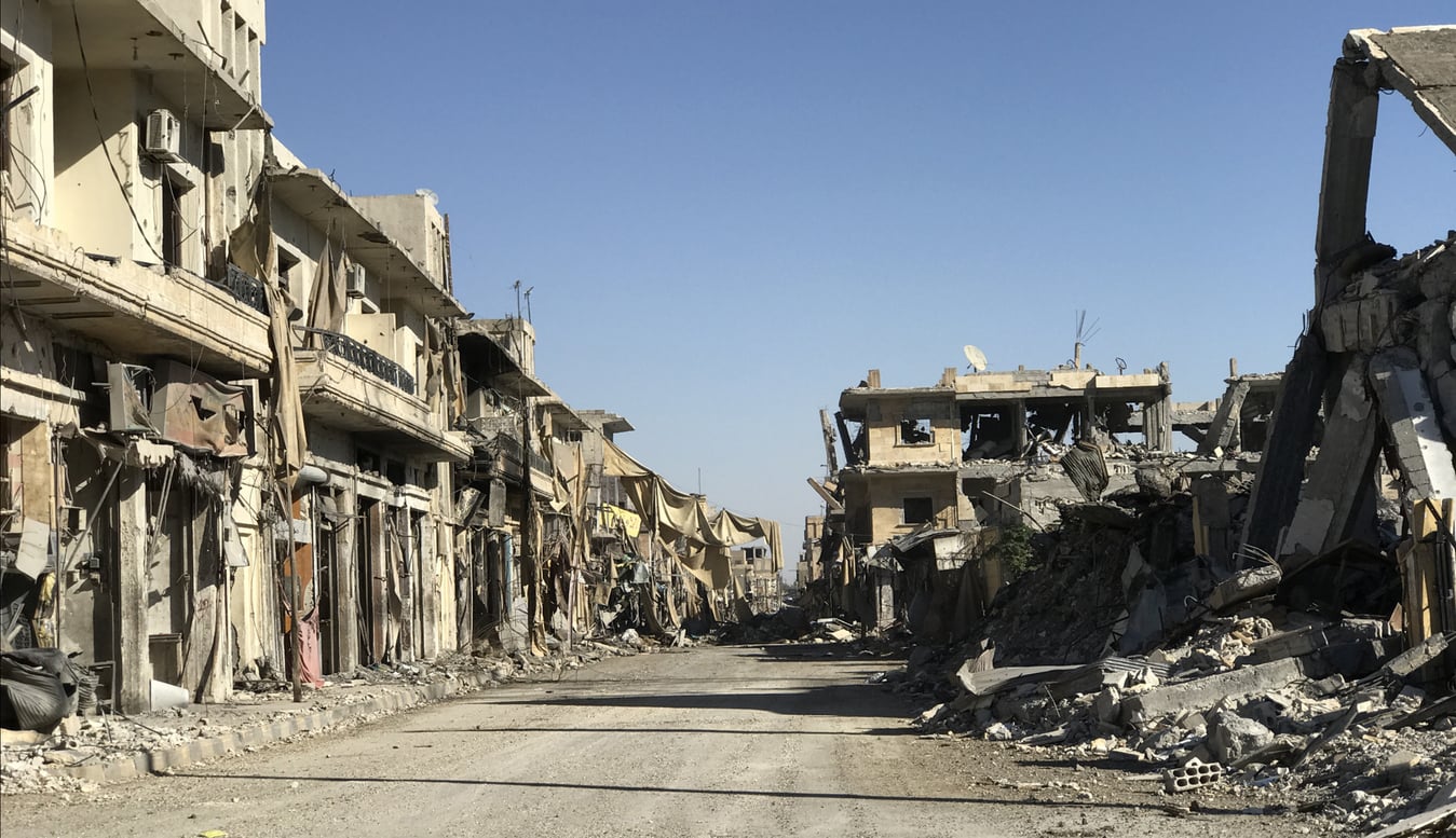 A deserted street lined with heavily damaged and partially collapsed buildings under a clear blue sky, showing extensive destruction and debris—one of the many haunting sights in areas that rank high on the list of Places Travelers Are Warning Against Going In 2026.