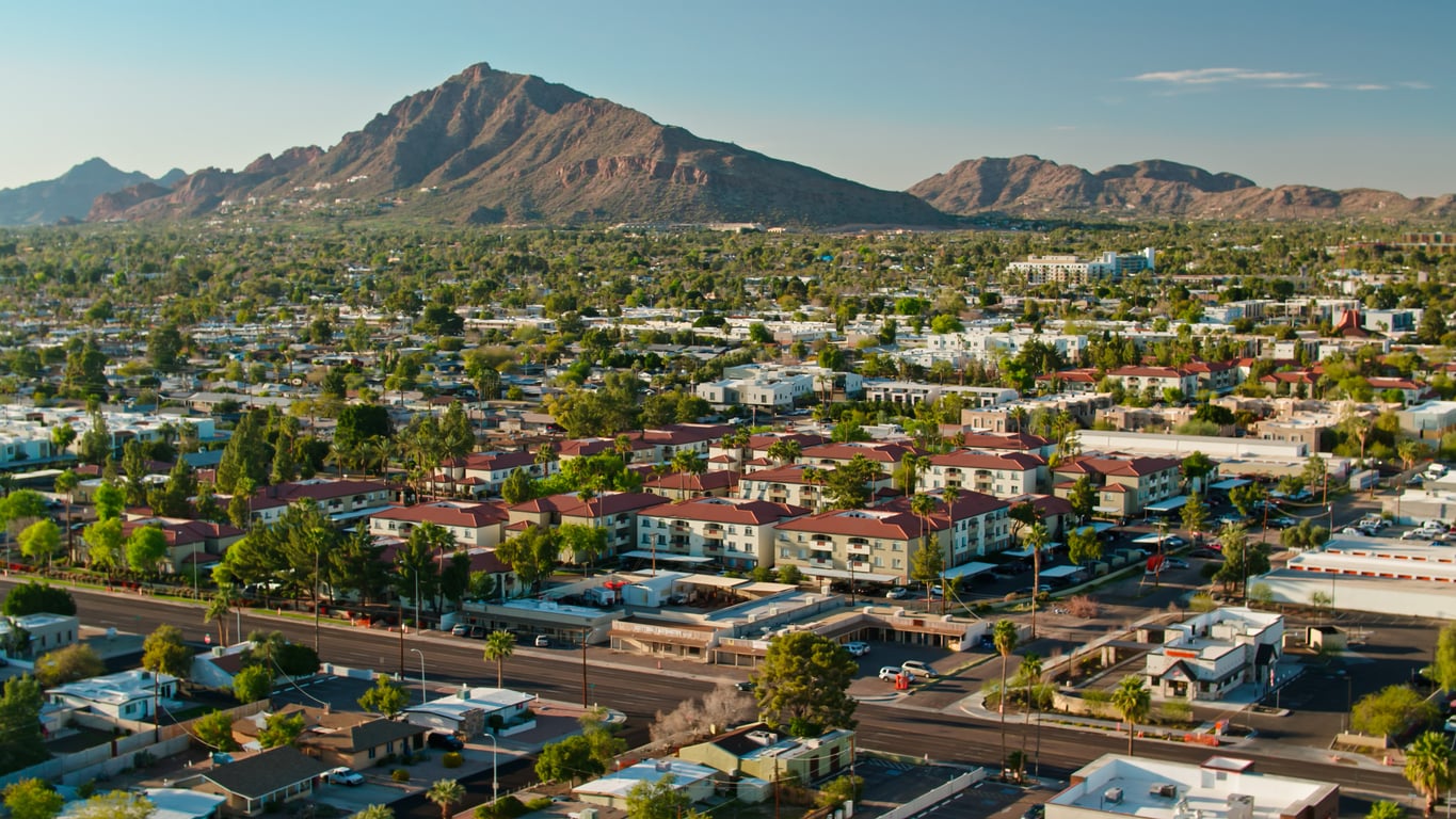 Aerial view of a suburban city with houses, trees, and buildings in the foreground, and a large mountain range in the background under a clear blue sky—an inspiring scene that reminds us of the possibilities that continue to unfold after age 50.