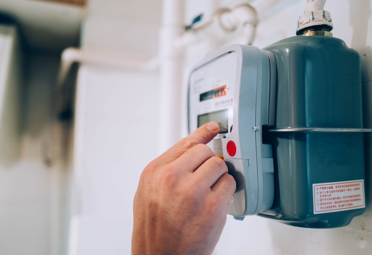 A person’s hand presses a button on a digital utility meter mounted on a wall, likely checking gas or energy usage in a home.