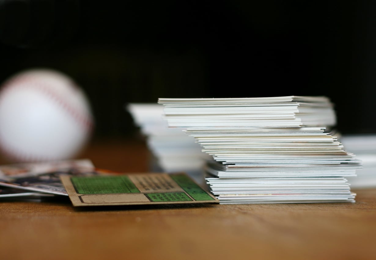 Stacks of baseball cards on a wooden surface with a blurred baseball in the background.