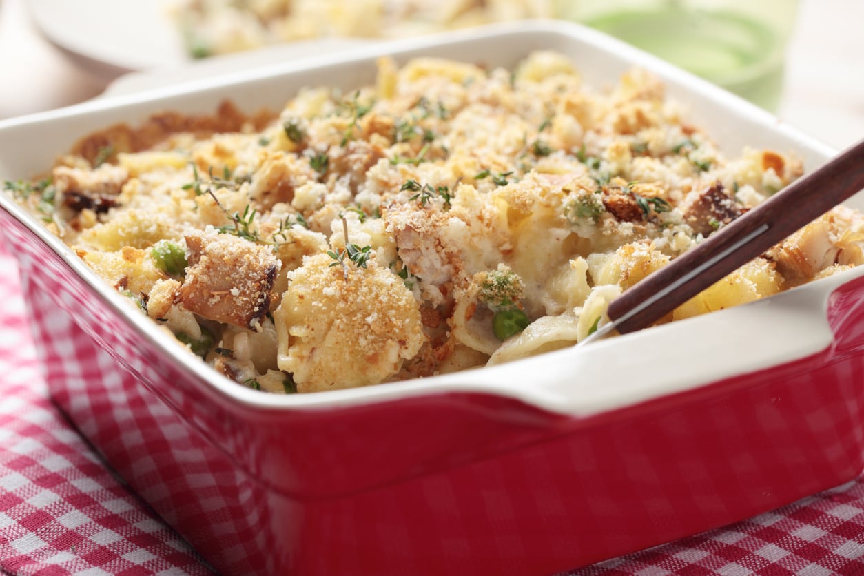 A close-up of a baked casserole with a golden breadcrumb topping in a red dish, resting on a red and white checkered cloth—a comforting classic reminiscent of the hearty meals middle-class moms made.