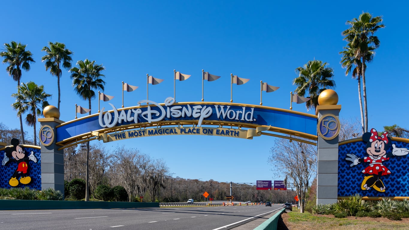 The Walt Disney World entrance sign features Mickey and Minnie Mouse on either side, with palm trees and a clear blue sky in the background—a cheerful sight that stands out even as Travel Destinations Boomers Are Skipping continue to shift.