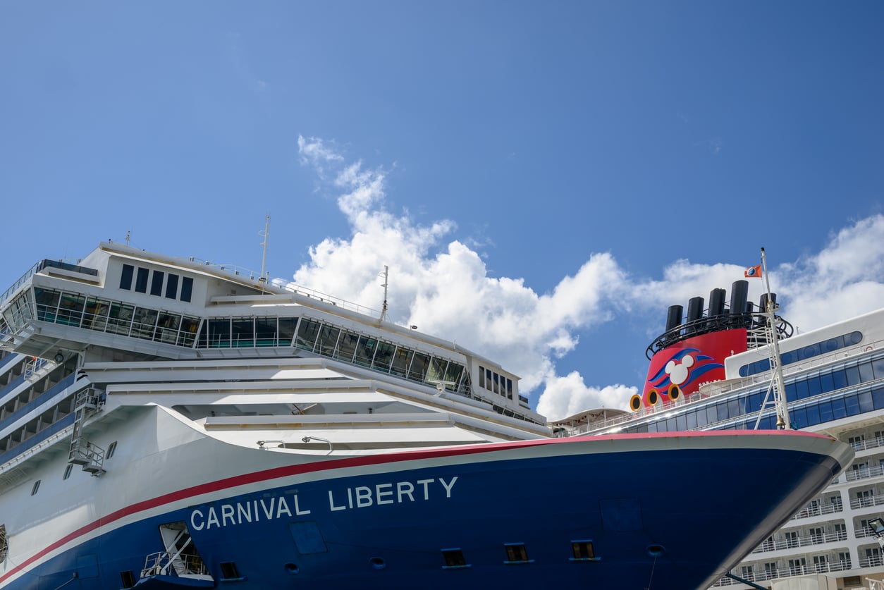 Close-up of the Carnival Liberty cruise ship’s bow—part of Carnival’s renowned cruise lines—with part of another cruise ship in the background, set against a blue sky with scattered clouds.