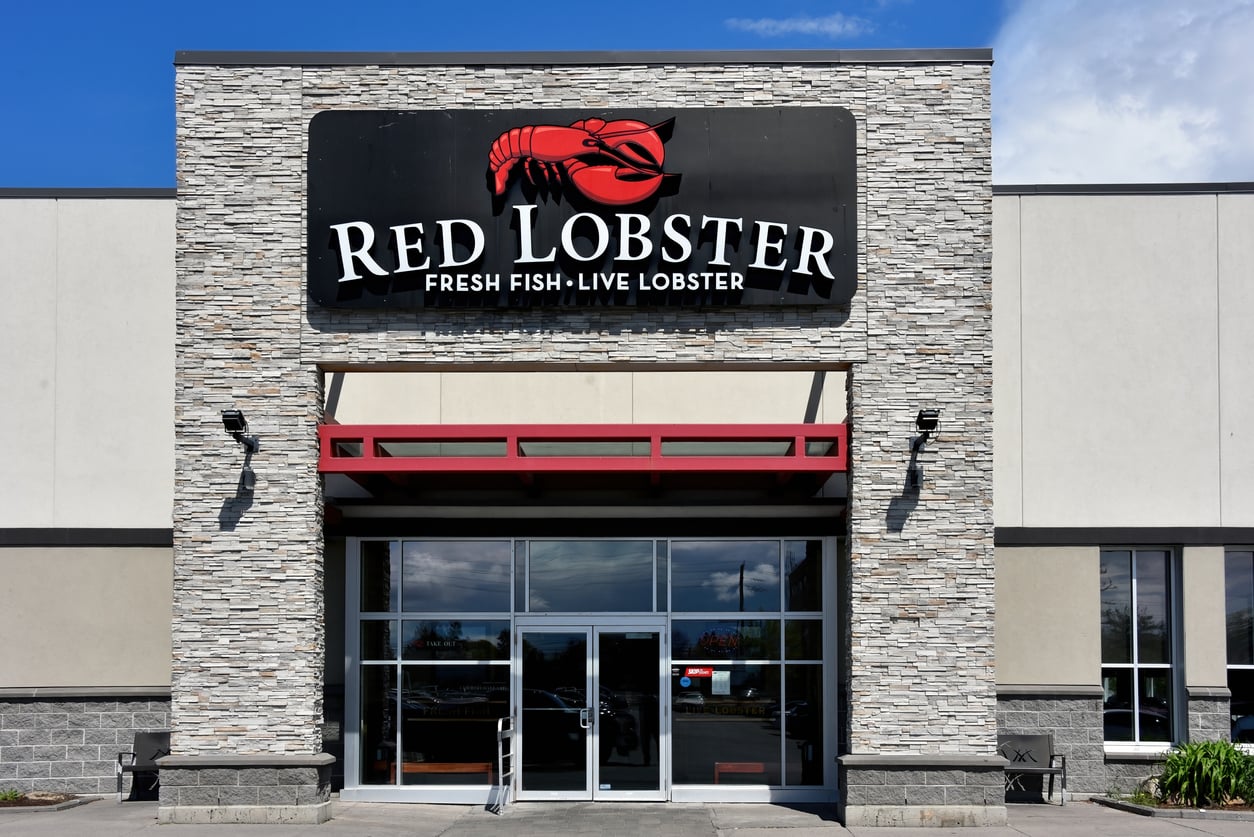 Exterior of a Red Lobster restaurant with stone facade, large sign featuring a red lobster logo, and the words “Fresh Fish • Live Lobster” above the entrance.