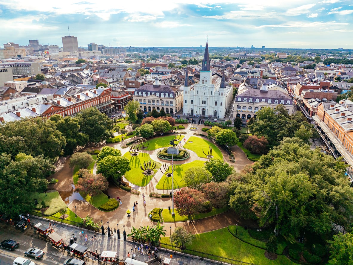 Aerial view of Jackson Square in New Orleans, one of the city’s most nostalgic travel destinations, featuring St. Louis Cathedral, lush gardens, paths, and surrounding historic buildings under a partly cloudy sky.