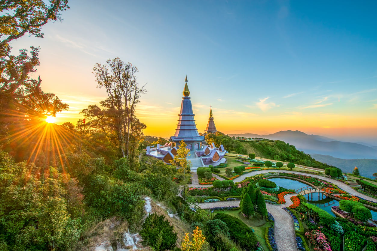 Two pagodas sit on a lush hilltop surrounded by gardens at sunrise, with golden sunlight streaming through trees and misty mountains in the background—a picturesque scene among the travel spots boomers are learning to love.