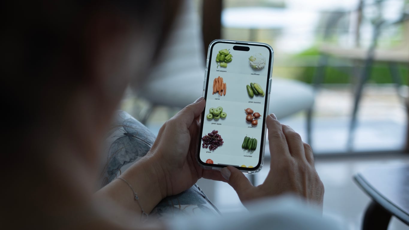 A person holds a smartphone displaying an online grocery shopping app with various fruits and vegetables shown on the screen.
