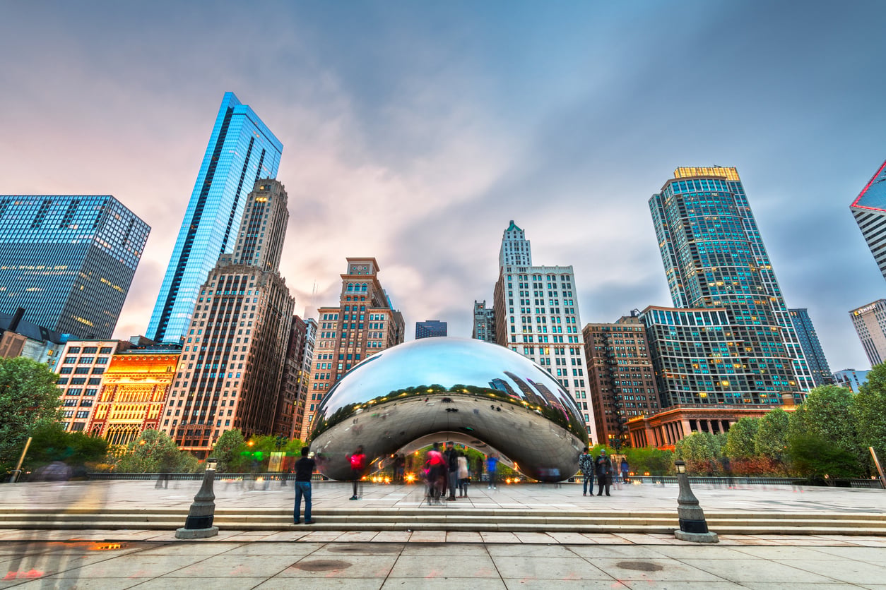 The Cloud Gate sculpture, known as “The Bean,” reflects the Chicago skyline at sunset, with people gathered around in Millennium Park—one of the city’s most iconic vacation spots.