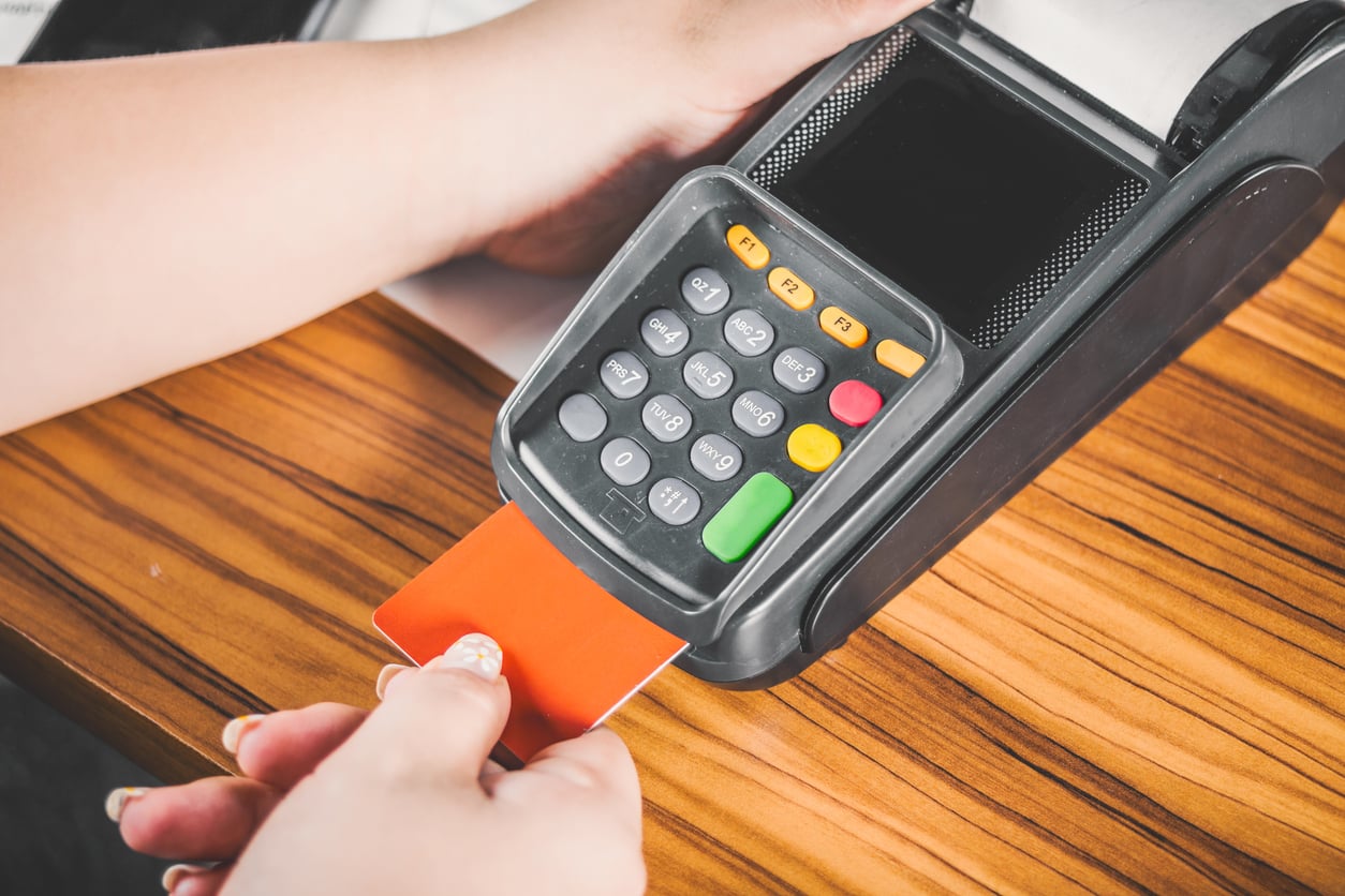 A person inserts a red credit card into a card reader on a wooden table, preparing to make a payment.