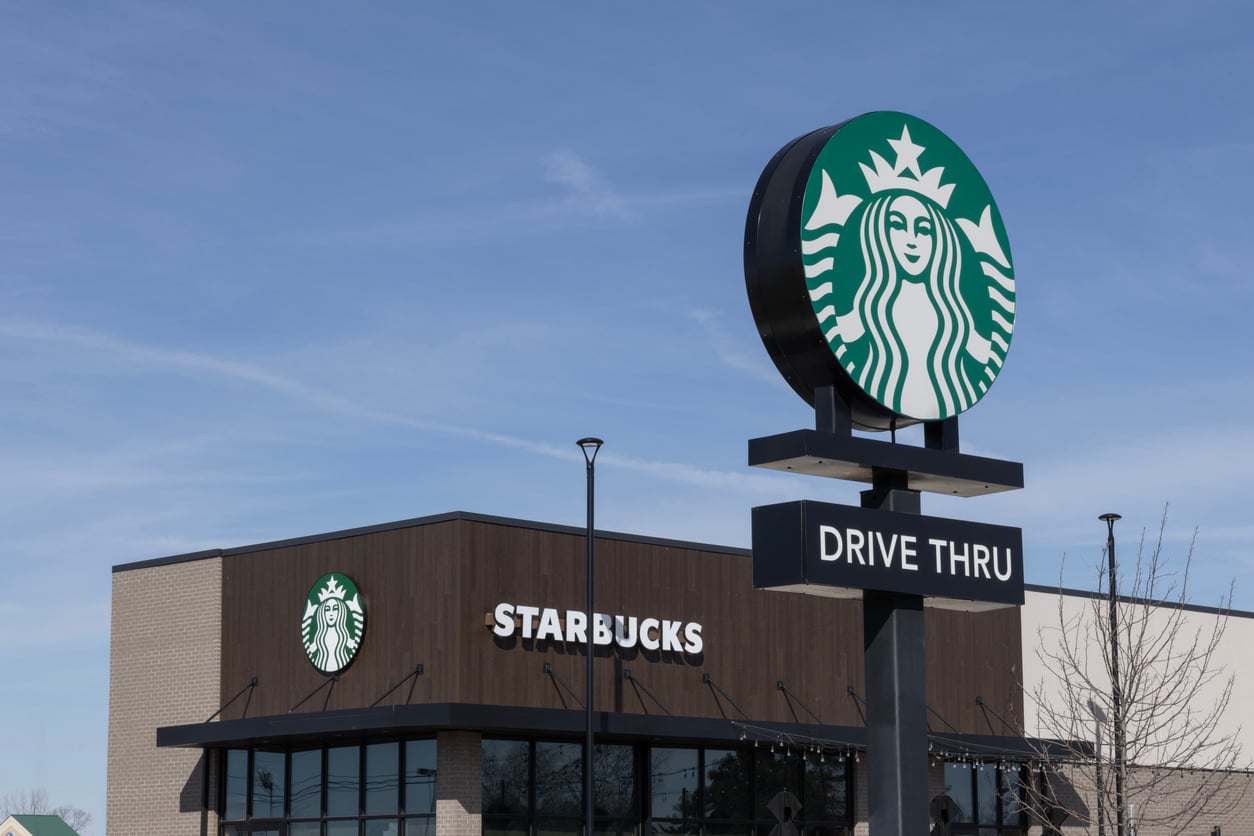 A Starbucks building with a large drive thru sign featuring the Starbucks logo in front, under a clear blue sky.