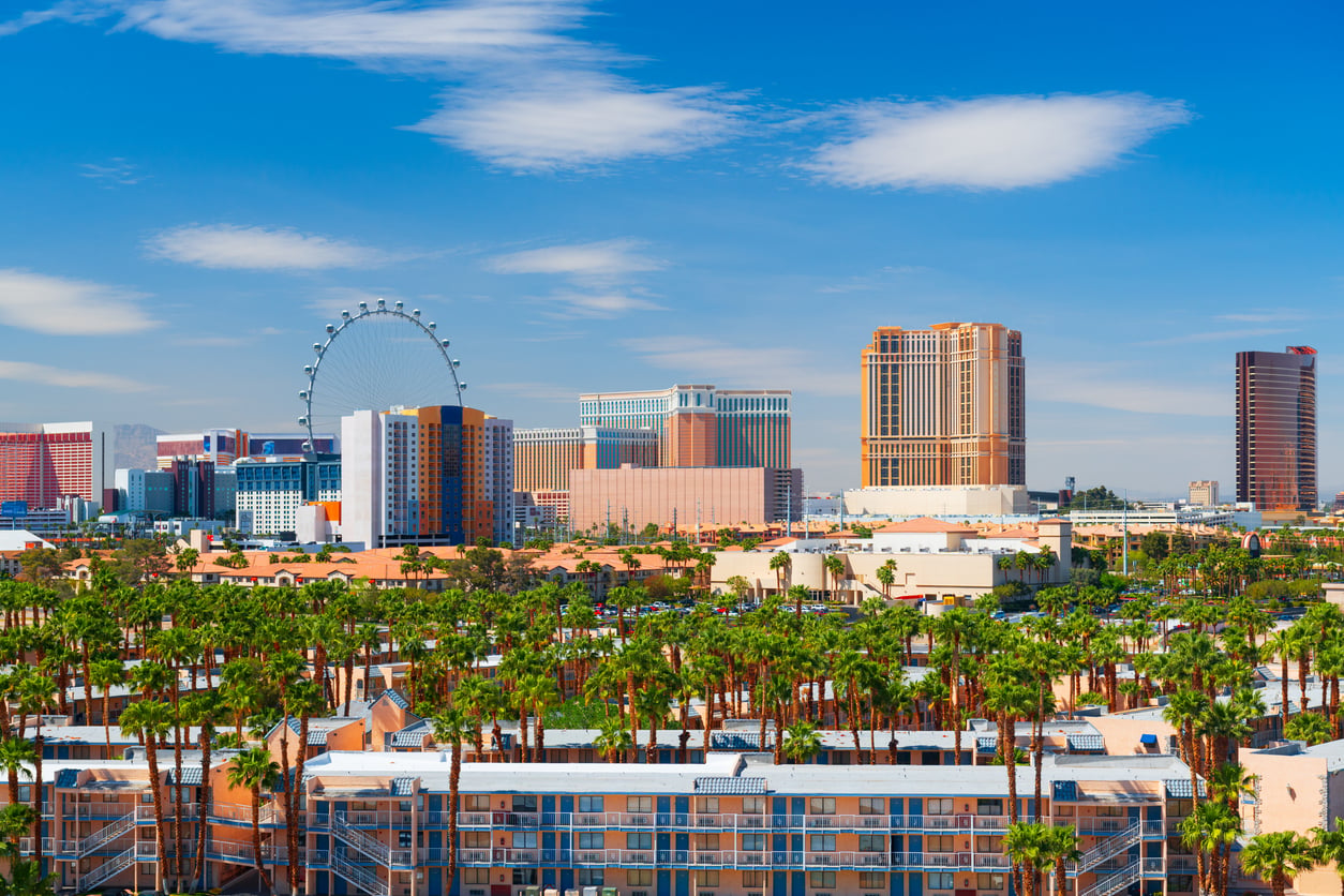 Explore the vibrant Las Vegas cityscape with palm trees, iconic hotels, and the towering High Roller Ferris wheel under a bright blue sky with scattered clouds—an unforgettable scene that perfectly captures some of the unique facts about Las Vegas.