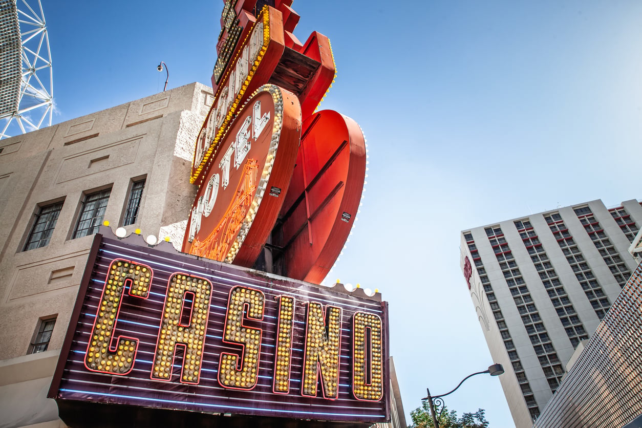 A vintage neon casino sign with yellow lights is mounted on a building, set against a modern high-rise and clear blue sky in the background—a scene that perfectly captures the vibrant contrast often seen in images highlighting facts about Las Vegas.