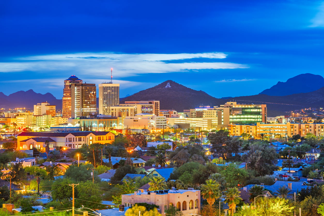 Cityscape of Tucson, Arizona at dusk, with illuminated buildings, the surrounding mountains, and a hill featuring a large white “A” visible in the background under a blue sky—one of the travel spots boomers are learning to love for its vibrant scenery and unique Southwestern charm.