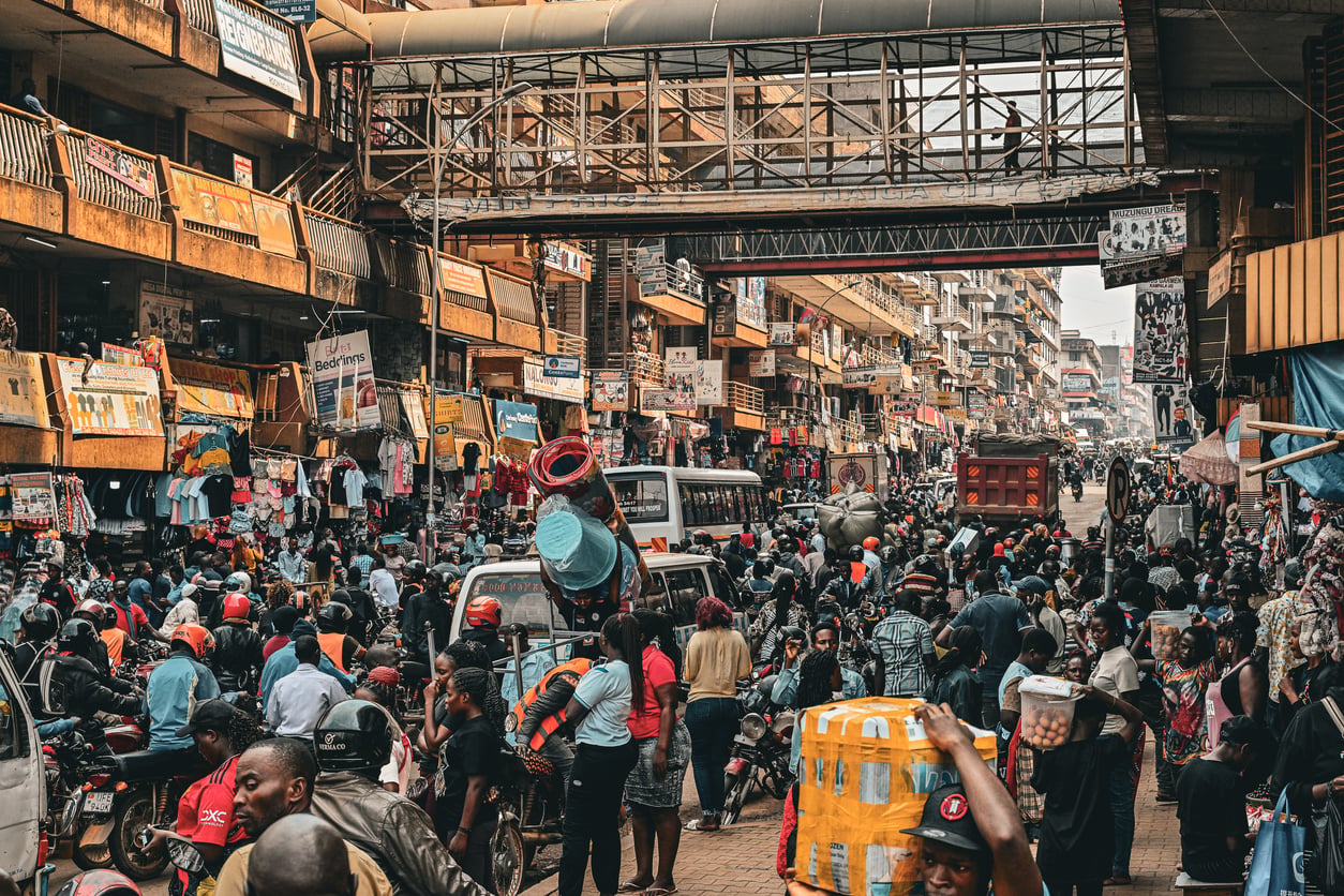 Busy urban market scene with large crowds, vendors, vehicles, and motorbikes. Tall buildings with shops and signs line the street, and an overhead walkway connects the structures above the bustling street—a lively snapshot that mirrors some of the Places Travelers Are Warning Against Going In 2026 due to their overwhelming energy and congestion.
