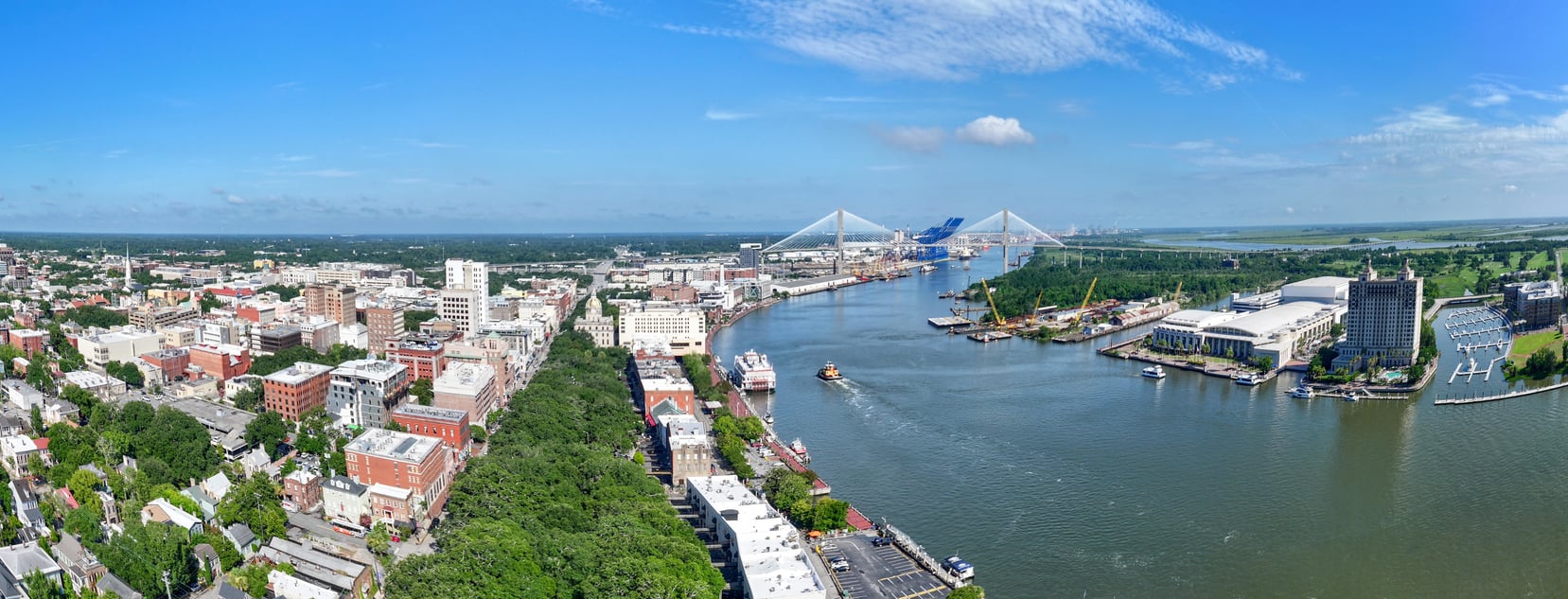 A panoramic view of a city with buildings along a river, boats on the water, a bridge in the distance, and a clear blue sky overhead—an inspiring scene that invites leisurely exploration, especially after age 50.