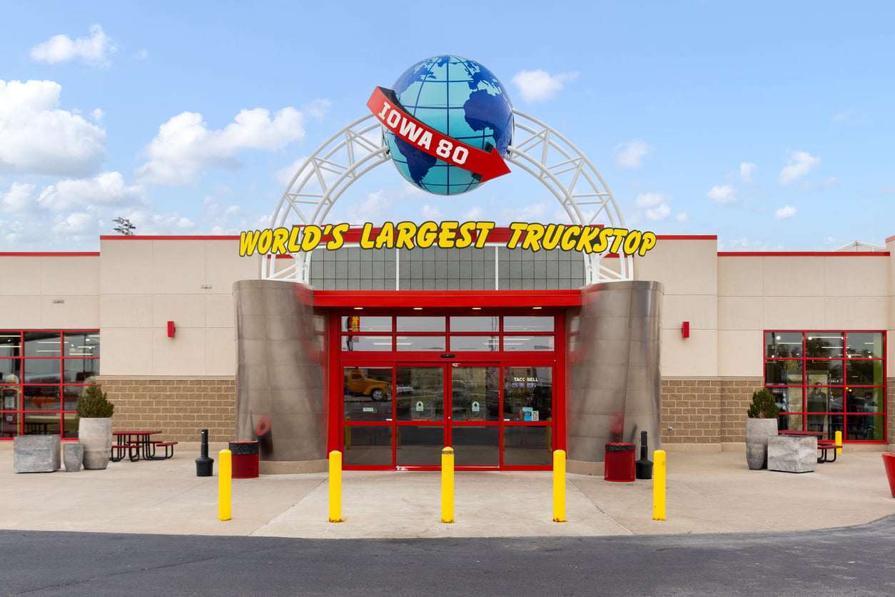 The entrance of the Iowa 80 Truckstop with a globe and red “Iowa 80” sign above the doors. Yellow letters say “World’s Largest Truckstop” on the front.