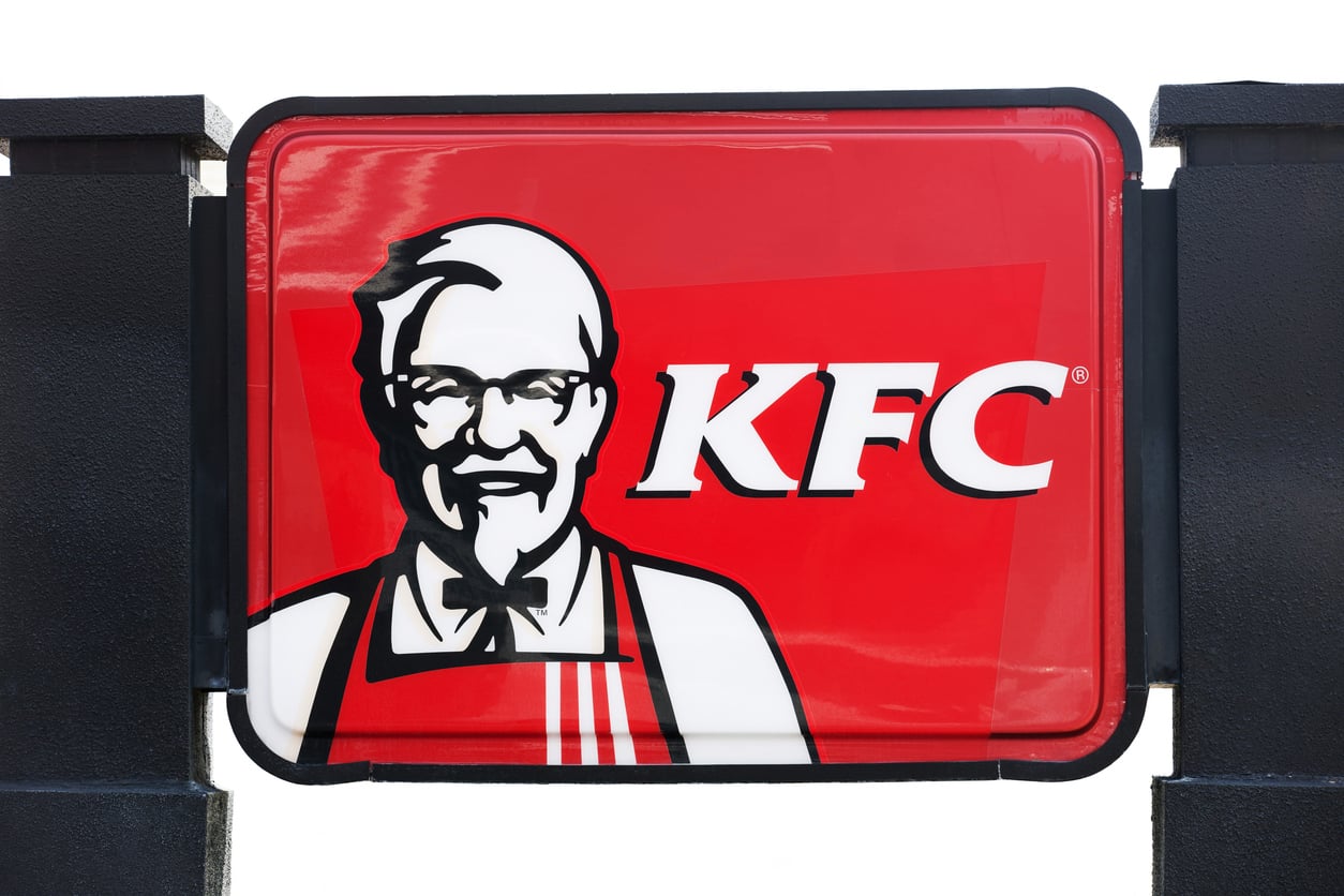 A red KFC sign featuring a white illustration of a man with glasses, a goatee, and a bow tie is positioned next to the bold white letters “KFC,” serving up another example of Wild Fast-Food Facts in iconic branding.