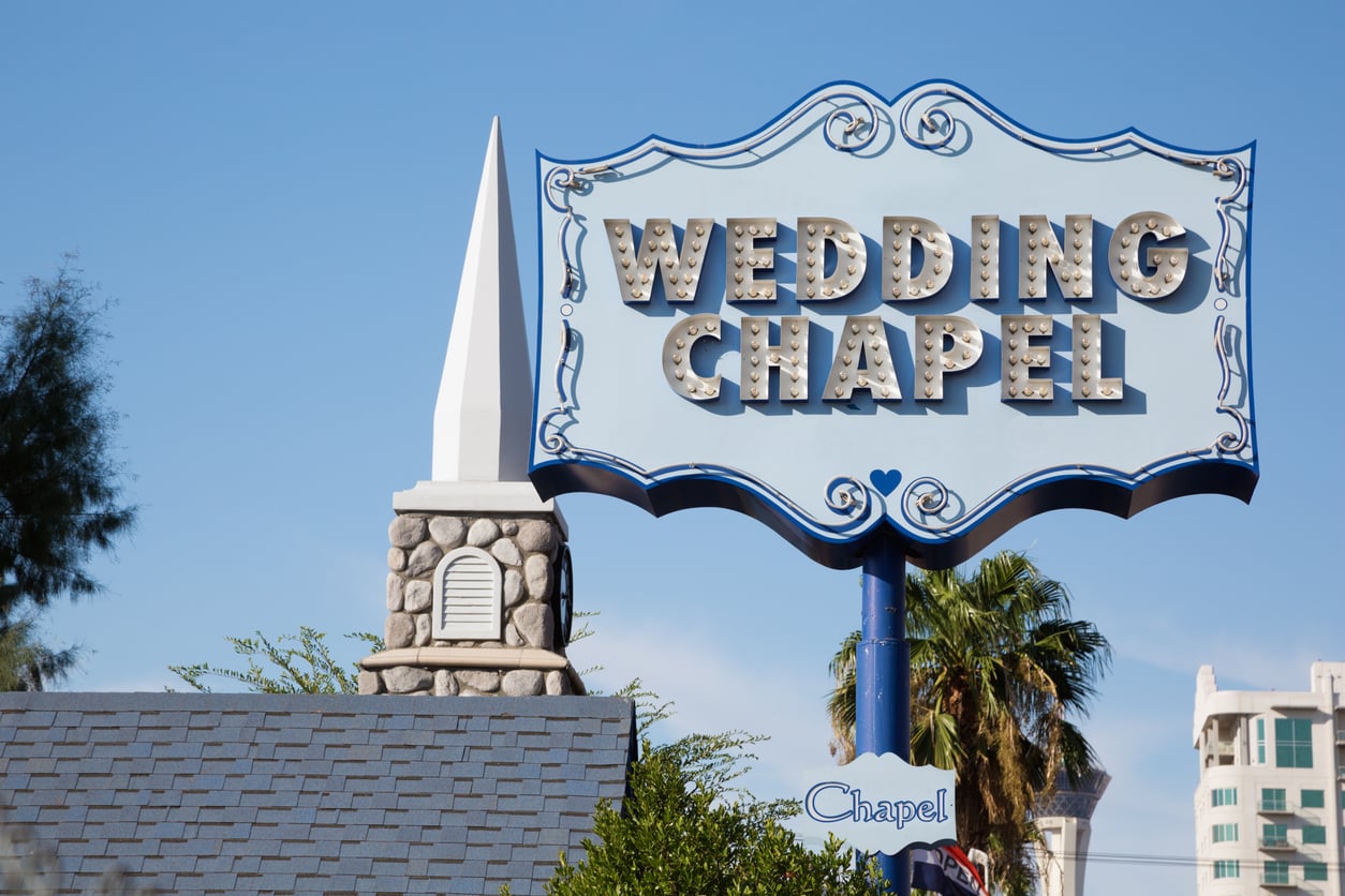 A vintage “Wedding Chapel” sign with lights stands next to a small chapel building with a white steeple, palm trees, and a blue sky in the background—capturing the iconic charm seen in many Facts About Las Vegas.