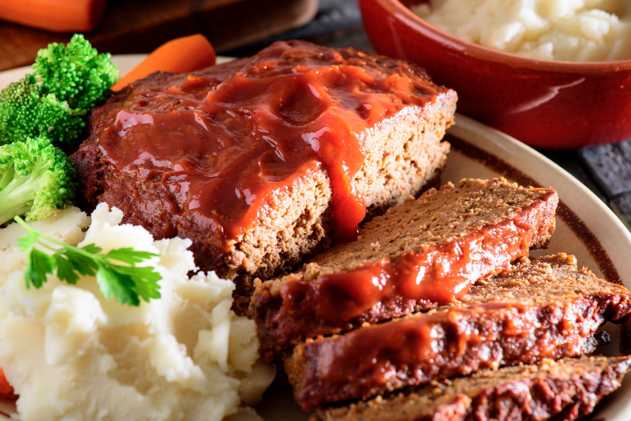 Close-up of sliced meatloaf topped with ketchup, served with mashed potatoes and broccoli on a plate.