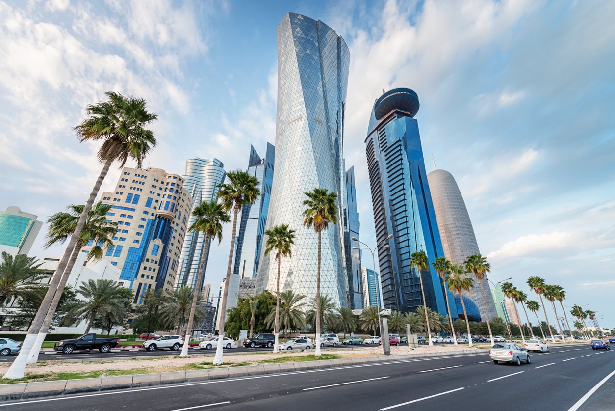 Modern skyscrapers and palm trees line a busy road under a partly cloudy sky in a cityscape featuring unique glass architecture and several cars on the street, offering a vibrant scene for visitors to explore—just be sure to stay updated on any travel restrictions and advisories before planning your trip.