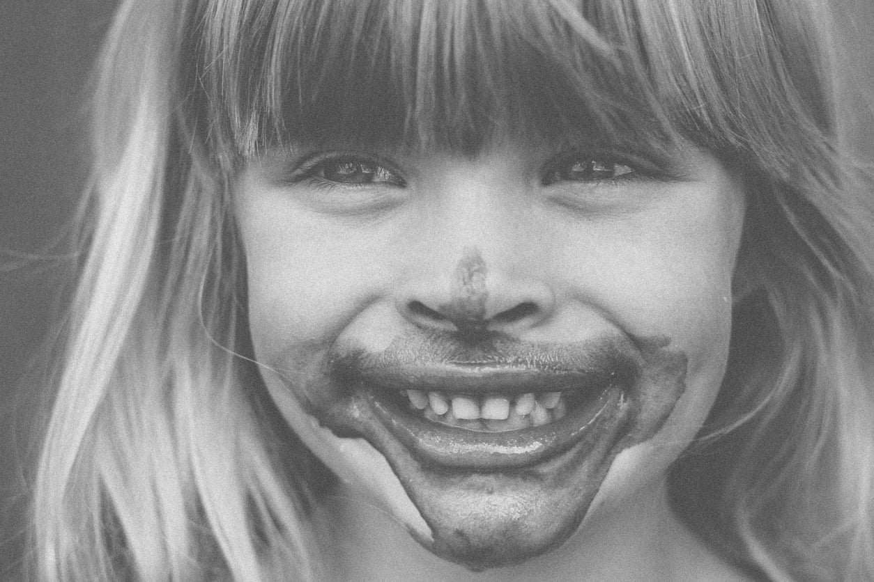 Smiling child with long hair and bangs, face covered in messy chocolate, looking directly at the camera. Black and white photo.