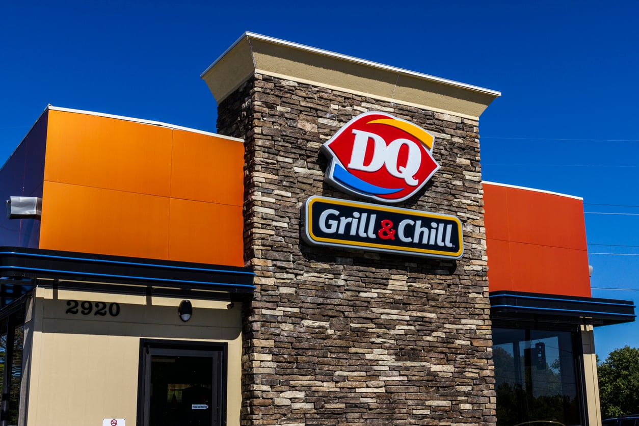 A Dairy Queen Grill & Chill restaurant with a stone facade, orange paneling, and the DQ logo displayed prominently under a clear blue sky—did you know this iconic spot is home to some Wild Fast-Food Facts?