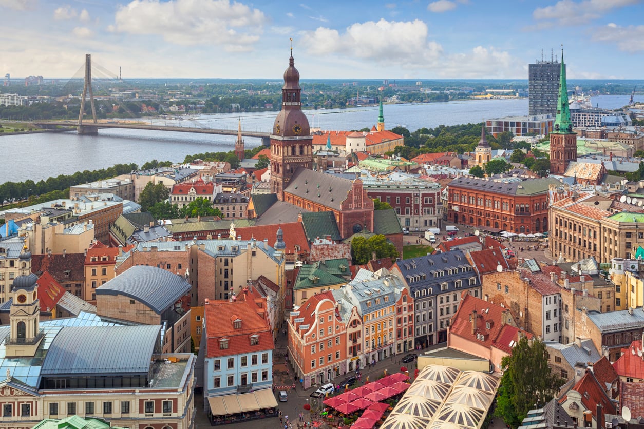 Aerial view of Riga, Latvia, showing colorful historic buildings, church towers, and a river with a bridge in the background under a partly cloudy sky—one of the travel spots boomers are learning to love for its charm and rich history.
