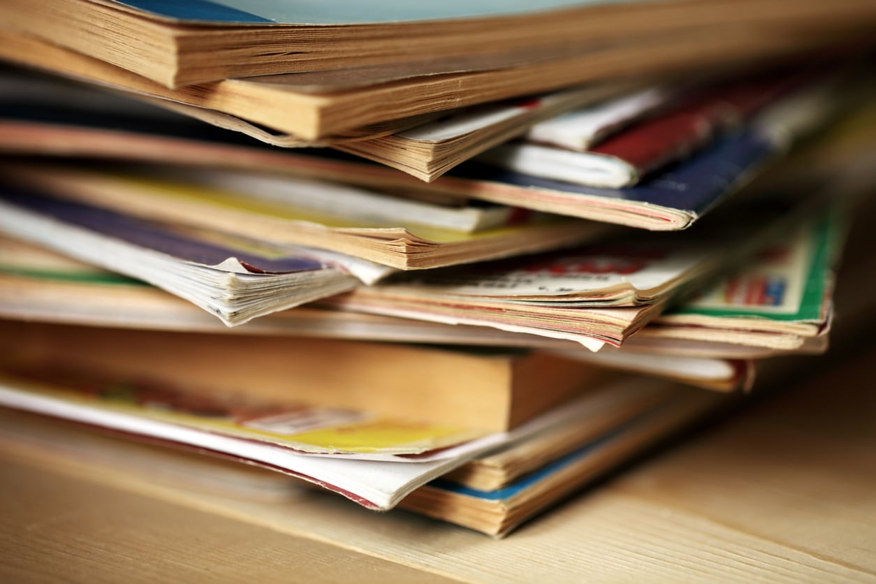 A close-up of a stack of old, colorful magazines and books with worn pages, sitting on a wooden surface.