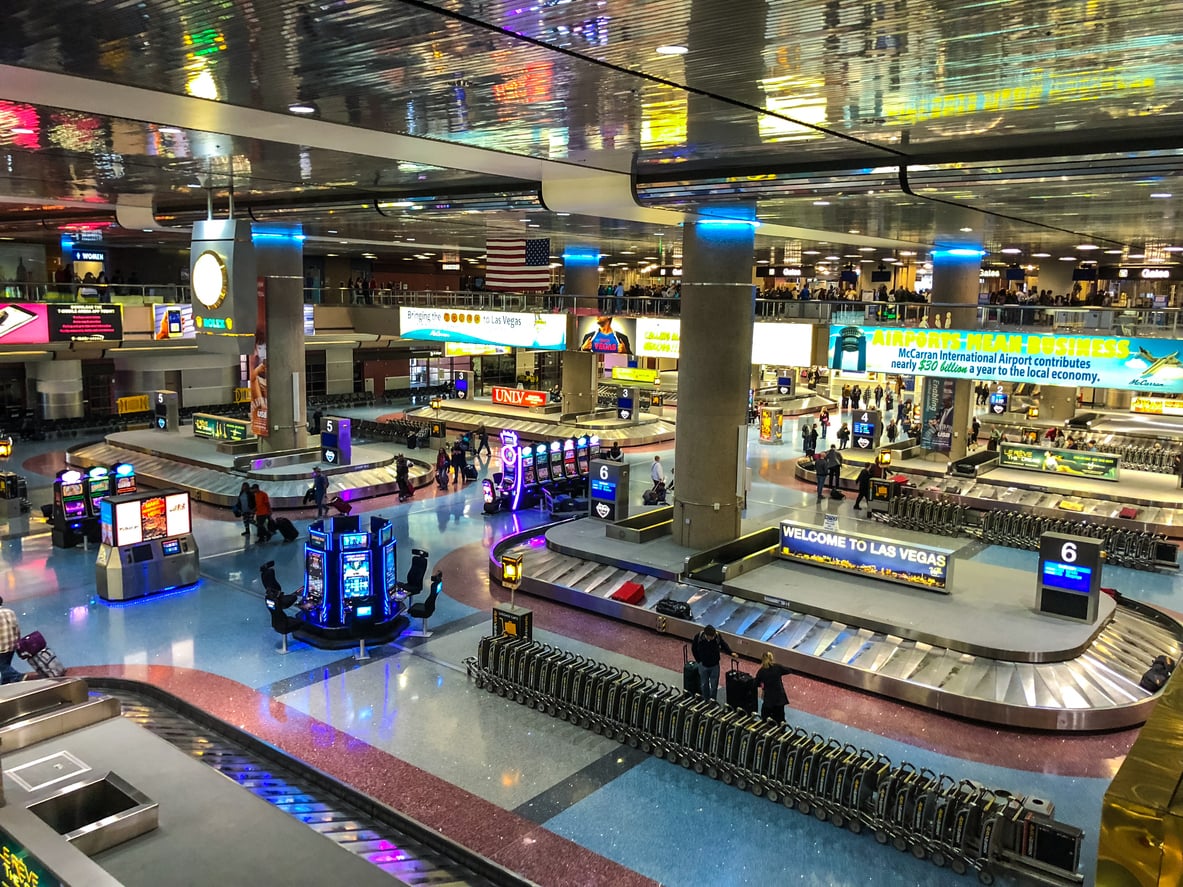 A brightly lit airport baggage claim area with luggage carousels, neon signs, and travelers collecting bags welcomes visitors with classic excitement. Signs read “Welcome to Las Vegas,” and slot machines are visible, offering a taste of the city’s famed gaming scene right away. The atmosphere is busy and vibrant, perfectly capturing one of the interesting facts about Las Vegas—it’s one of the few airports in the world where