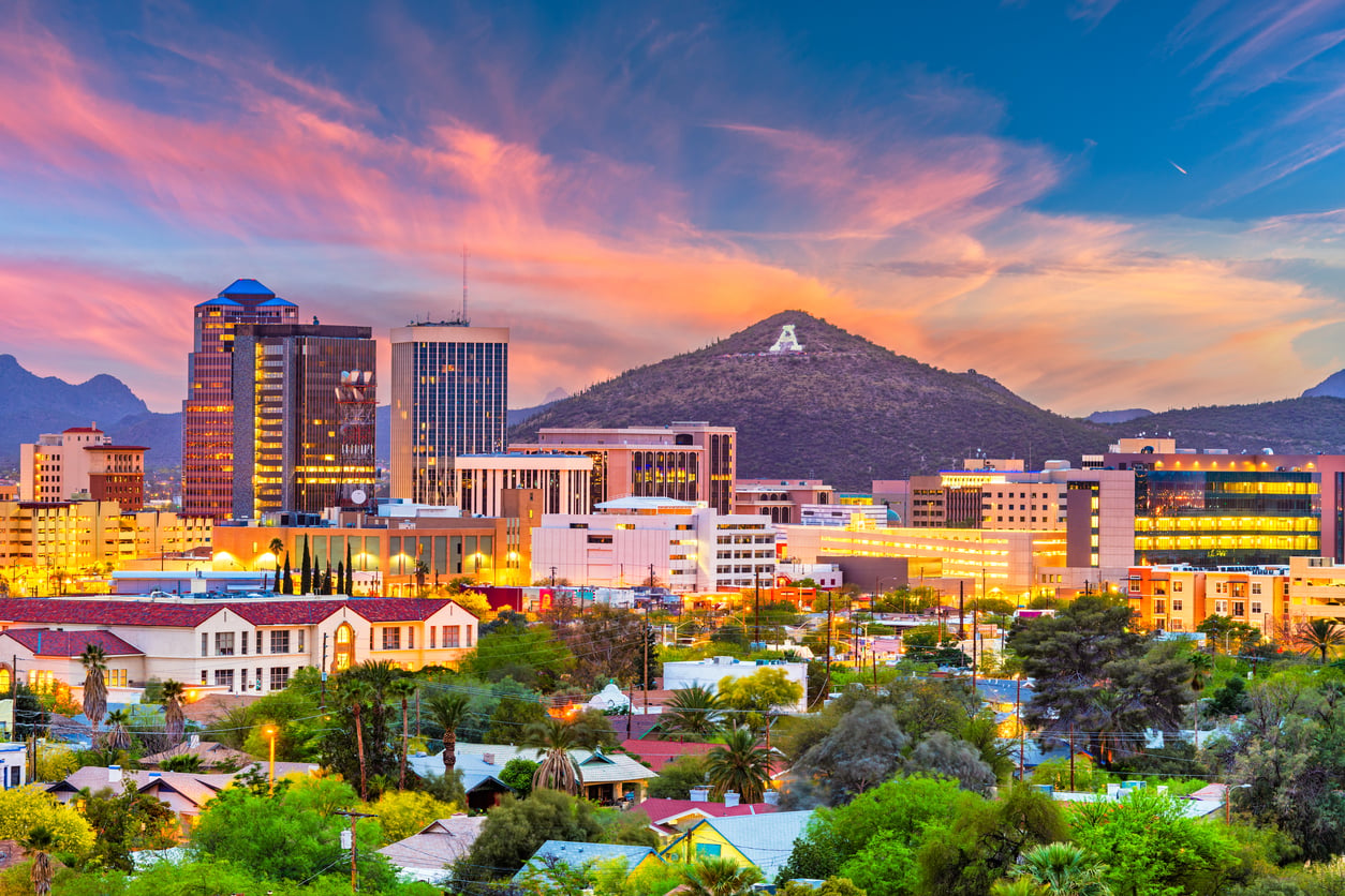 Downtown cityscape at sunset with a colorful sky, tall buildings, and a mountain in the background featuring a large white “A.” Trees and houses are visible in the foreground, highlighting one of the travel spots boomers are learning to love.