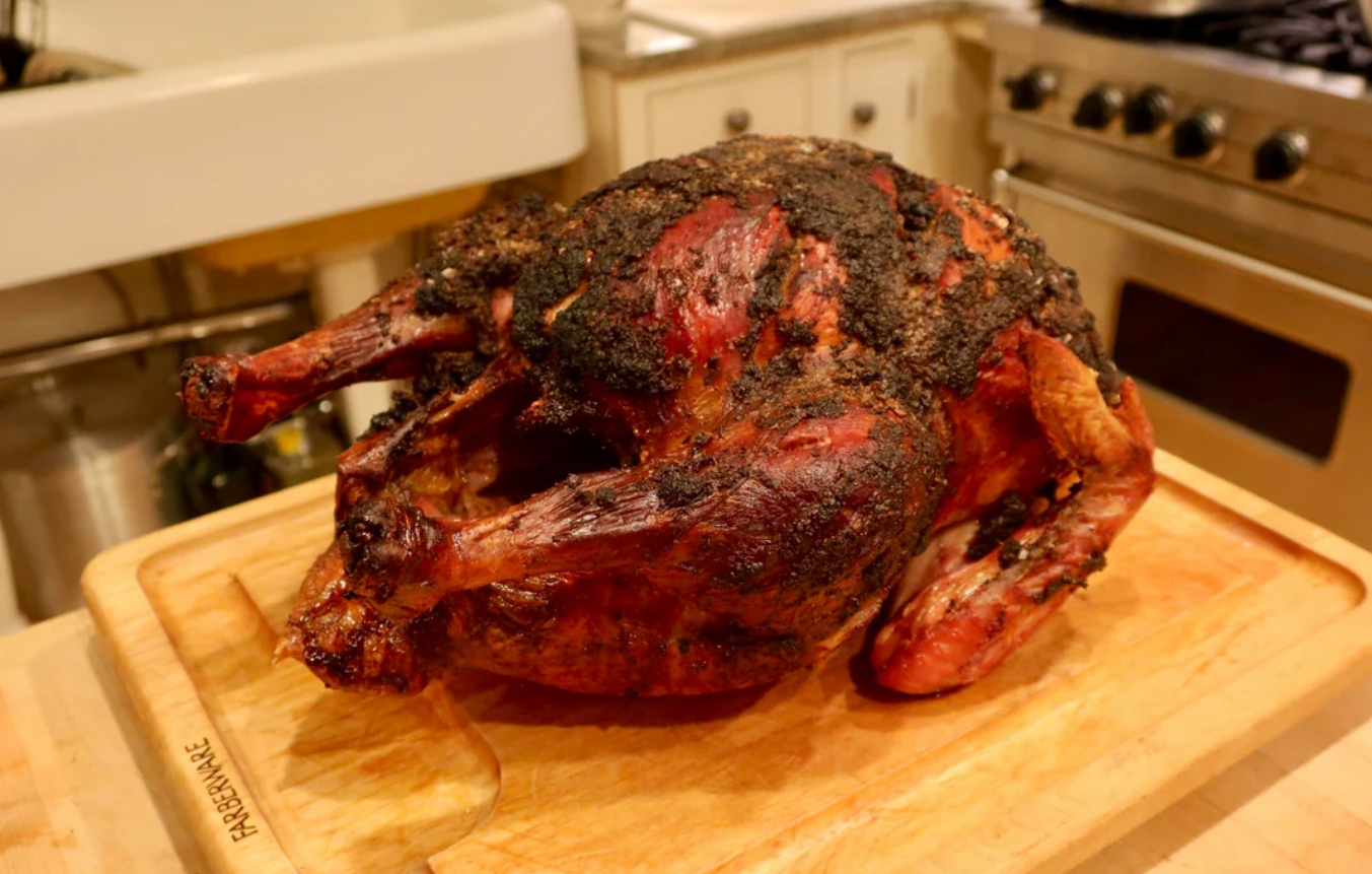 A whole roasted turkey with crispy, dark-browned skin sits on a wooden cutting board in a kitchen setting.