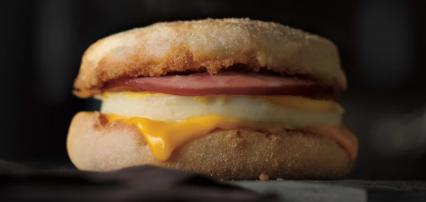 A breakfast sandwich with egg, a slice of ham, and melted cheese between two halves of an English muffin, set against a dark background—a classic morning favorite that’s earned its place among Wild Fast-Food Facts for its delicious simplicity and on-the-go appeal.