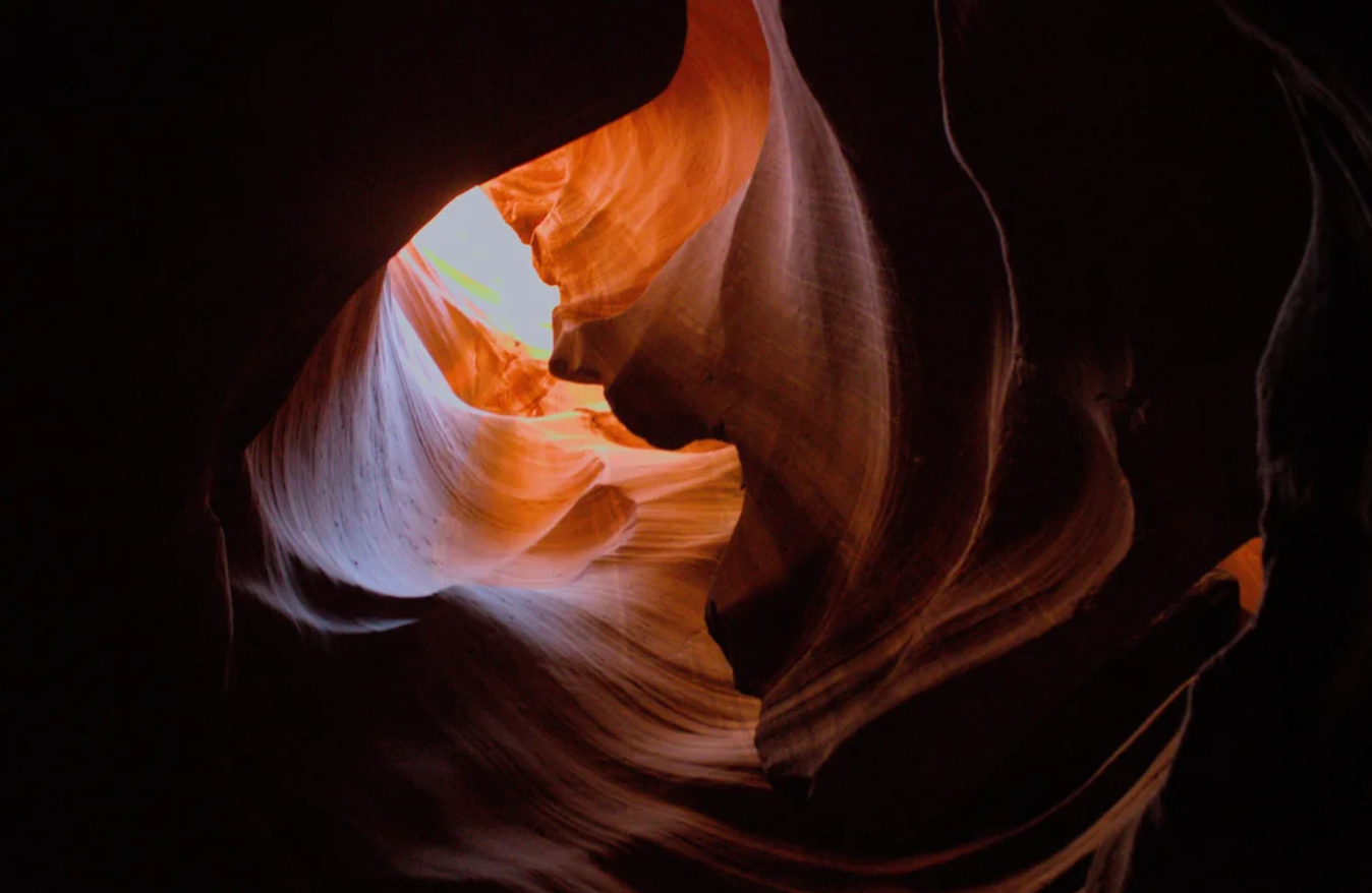 Narrow rays of sunlight illuminate smooth, swirling red and orange rock walls inside a dark slot canyon—a scene reminiscent of the breathtaking travel experiences that went viral for their otherworldly beauty.