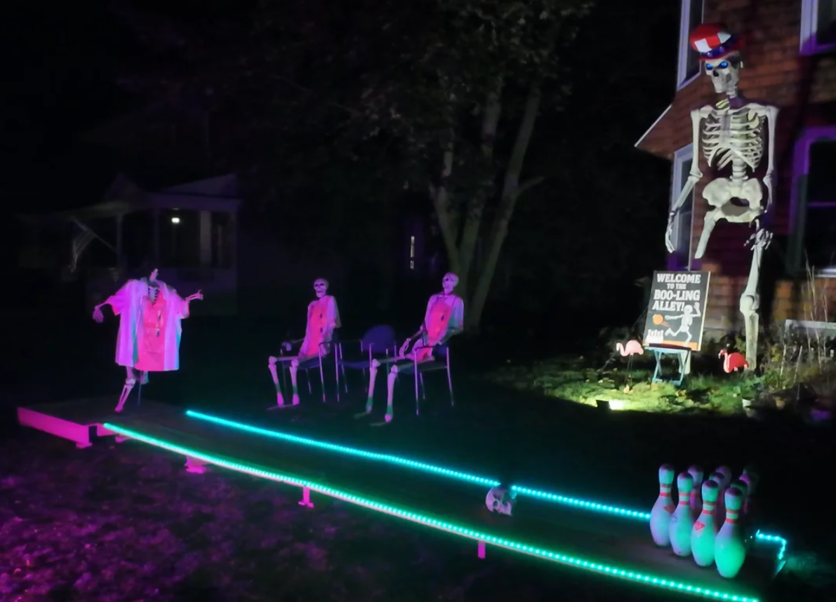 Three skeletons are set up like they’re bowling at night, making for the perfect Halloween yard decorations. Two sit as spectators while one stands to bowl. Neon lights line the lane, and the pins are ready. A large skeleton and a sign welcome visitors in the background, adding extra spooky charm to your festive display.