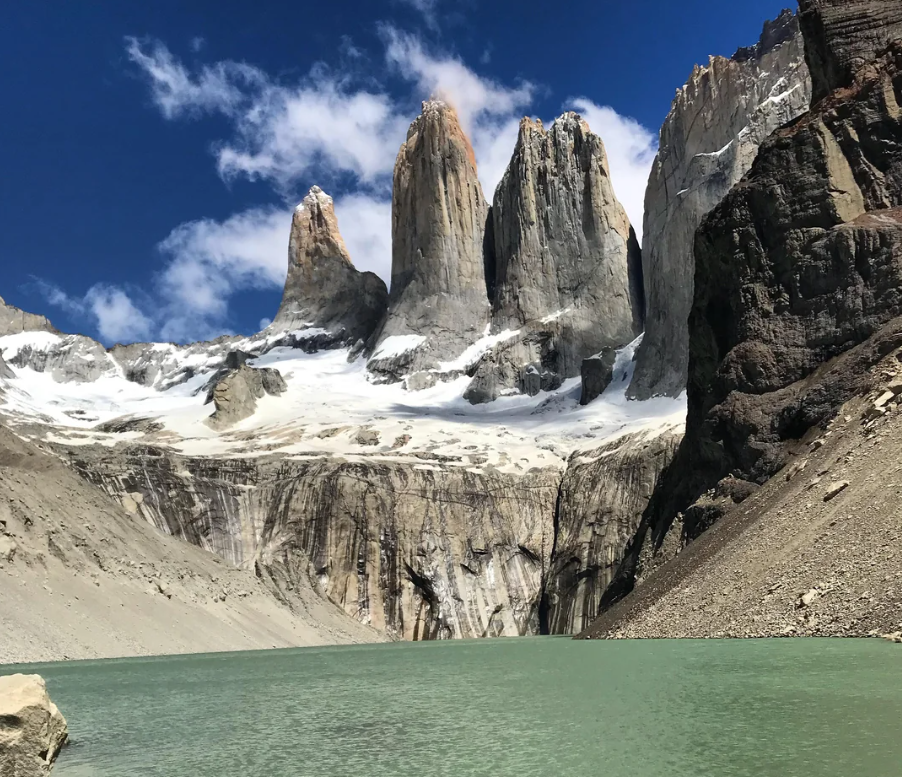 Turquoise lake in front of dramatic rocky peaks with some snow under a bright blue sky; steep cliffs rise on both sides, evoking the breathtaking beauty found in American National Parks.