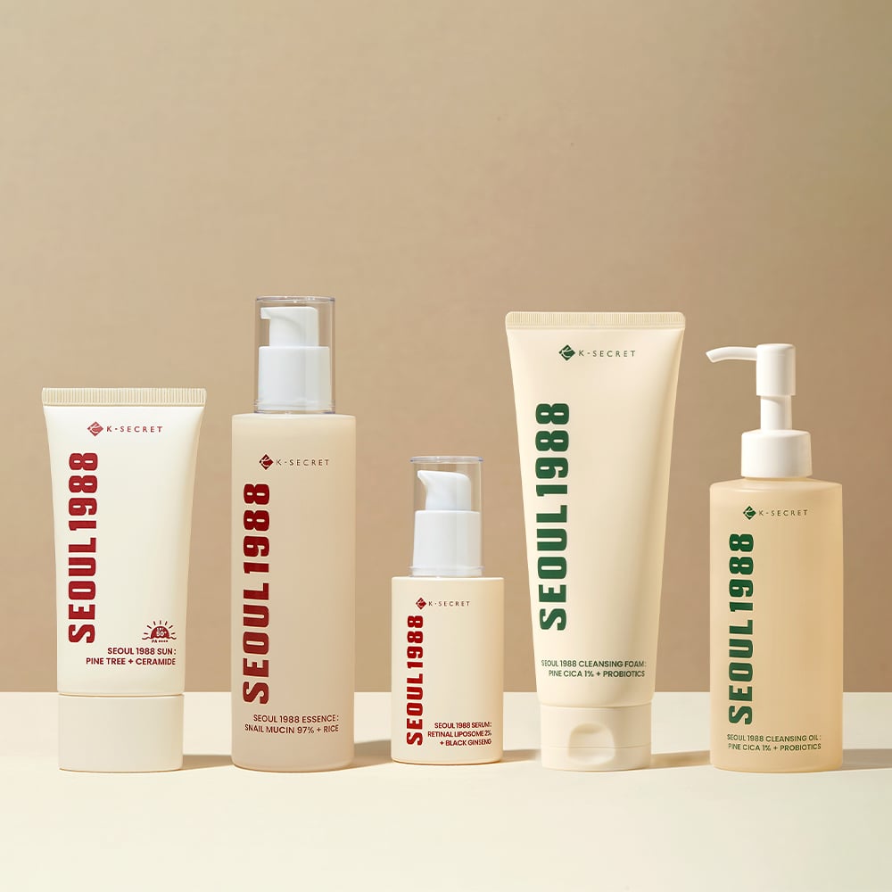 Five skincare products labeled “SEOUL 1988” in red and green text stand in a row on a beige surface against a light beige background. Each container is a different shape and size.