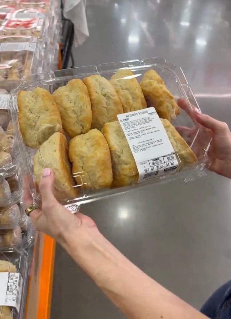 A person holds a clear plastic container of pastries in a grocery store aisle. The container has a white label and is filled with baked goods, likely croissants or similar bread items. New Costco products 2026.