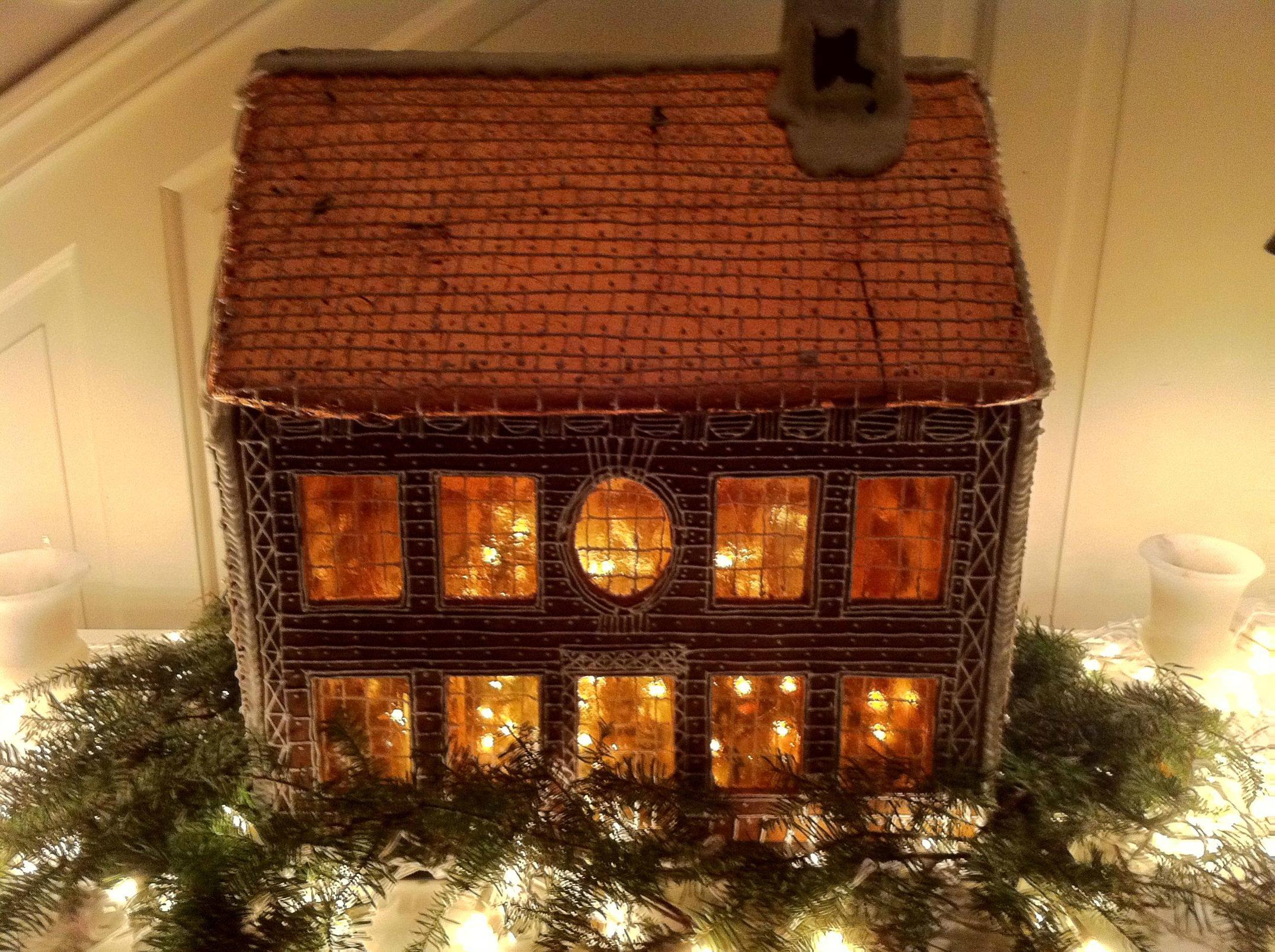 A small decorative house with lit windows sits among greenery and string lights, creating a warm, festive ambiance.