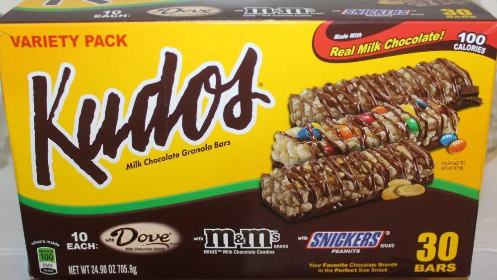 Box of Kudos variety pack granola bars with milk chocolate, featuring Dove, M&M’s, and Snickers flavors; 30 bars total, 100 calories each. Image shows the front packaging and bars with visible chocolate and toppings.