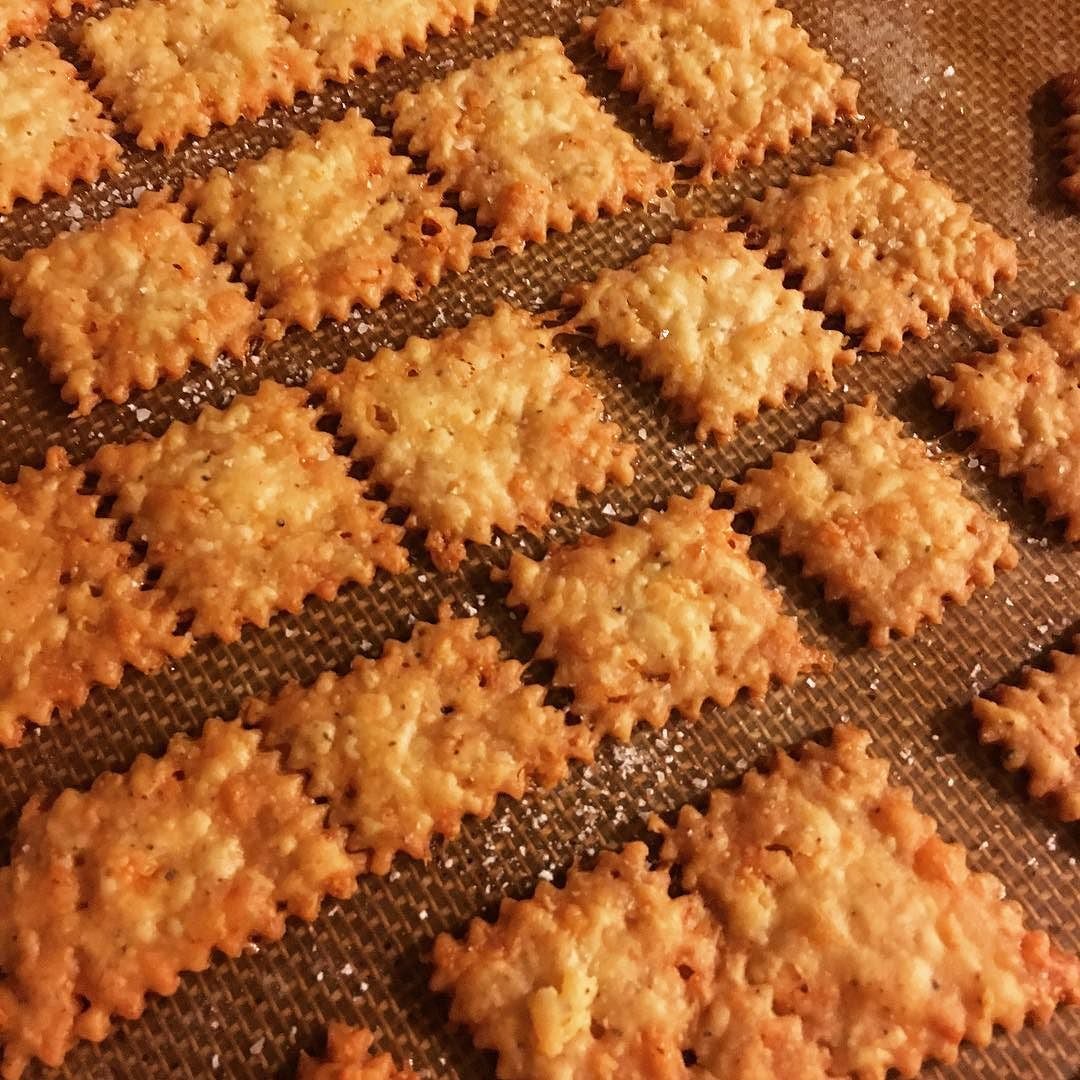Golden, homemade rectangular cheese crackers with zigzag edges are arranged in neat rows on a brown baking sheet.