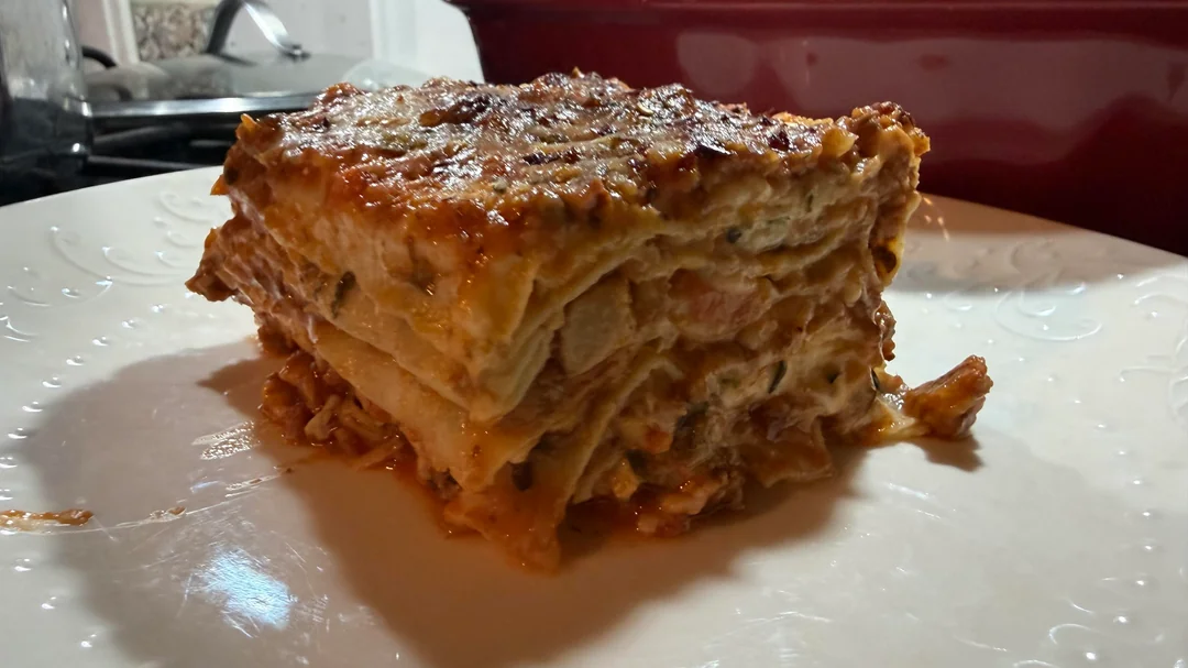 A close-up of a thick slice of lasagna with visible layers of pasta, meat, cheese, and sauce on a white plate.