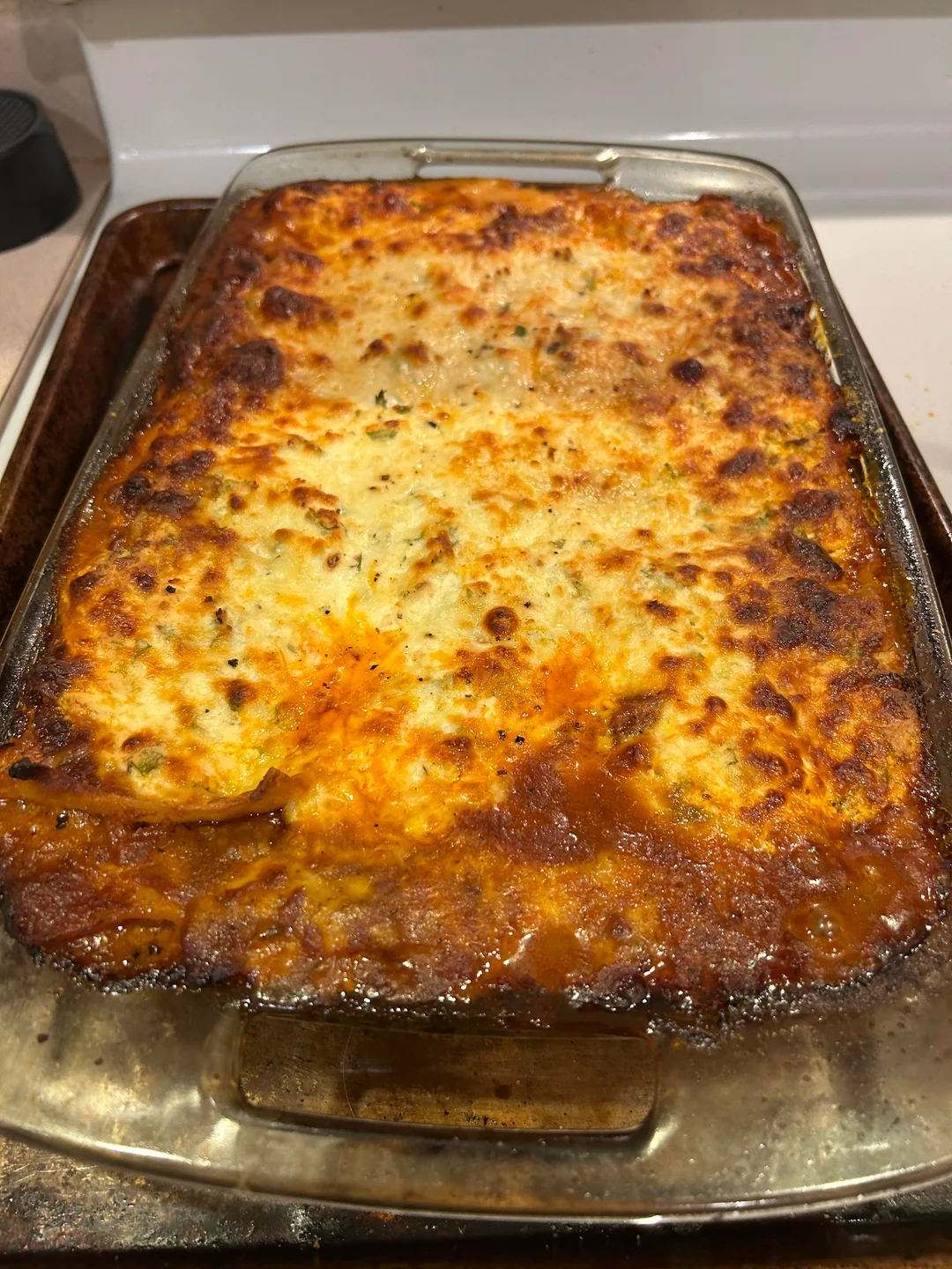 A glass baking dish filled with homemade lasagna, topped with a golden-brown, bubbly cheese layer, slightly crispy around the edges, resting on a baking sheet.