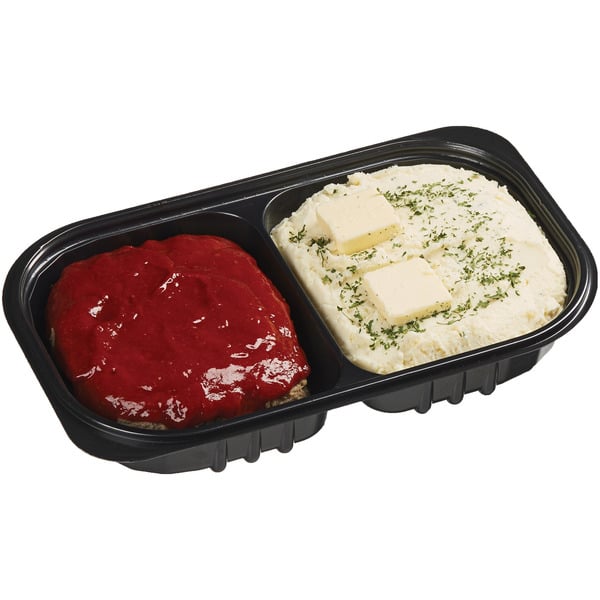 A black tray with two sections: one holds a serving of meatloaf topped with red sauce, the other contains mashed potatoes with three butter pats and green herb garnish.