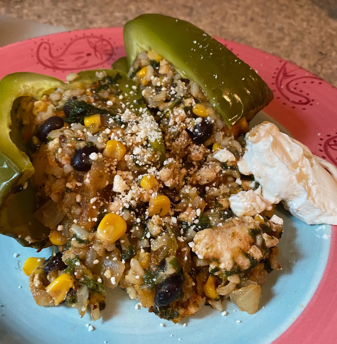 A green bell pepper stuffed with rice, black beans, corn, and herbs, topped with crumbled cheese, sits on a plate next to a dollop of sour cream.
