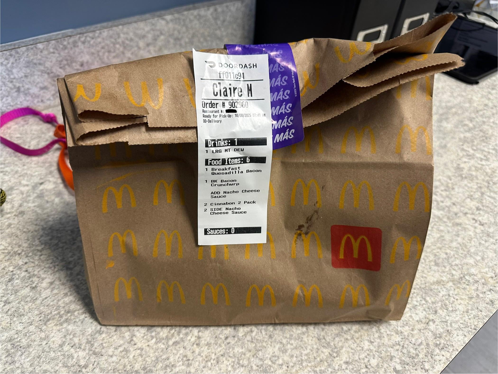 A brown McDonald’s takeout bag with an attached DoorDash receipt sits on a desk with office supplies in the background.