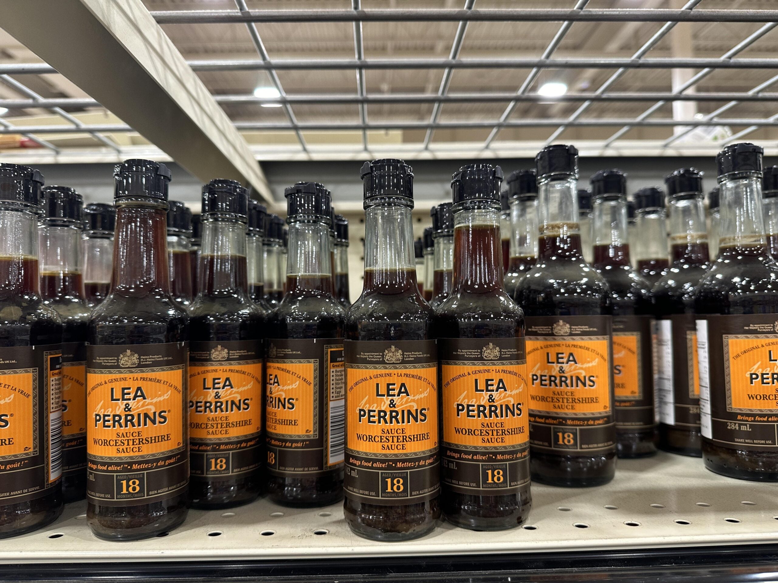 Several bottles of Lea & Perrins Worcestershire Sauce are lined up on a grocery store shelf, with metal shelving above and more bottles visible in the background.
