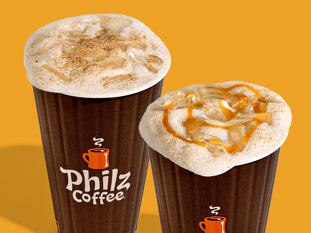 Two Philz Coffee cups filled with iced coffee drinks topped with foam. One has a sprinkle of cinnamon, while the other is drizzled with caramel and sprinkled with cinnamon, set against a solid yellow-orange background.